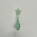 A small ceramic spoon-shaped ornament with a star handle and a hole at the top, glazed in a light mint green color, shown on a plain light gray background.