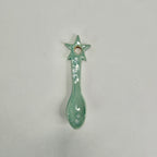 A small ceramic spoon-shaped ornament with a star handle and a hole at the top, glazed in a light mint green color, shown on a plain light gray background.