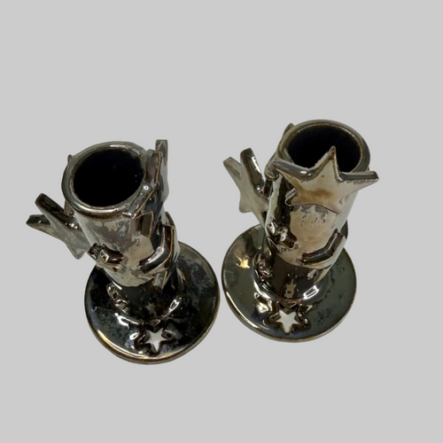 A pair of ceramic silver candle holders with star-shaped candle holders and round bases, shown on a plain light background.