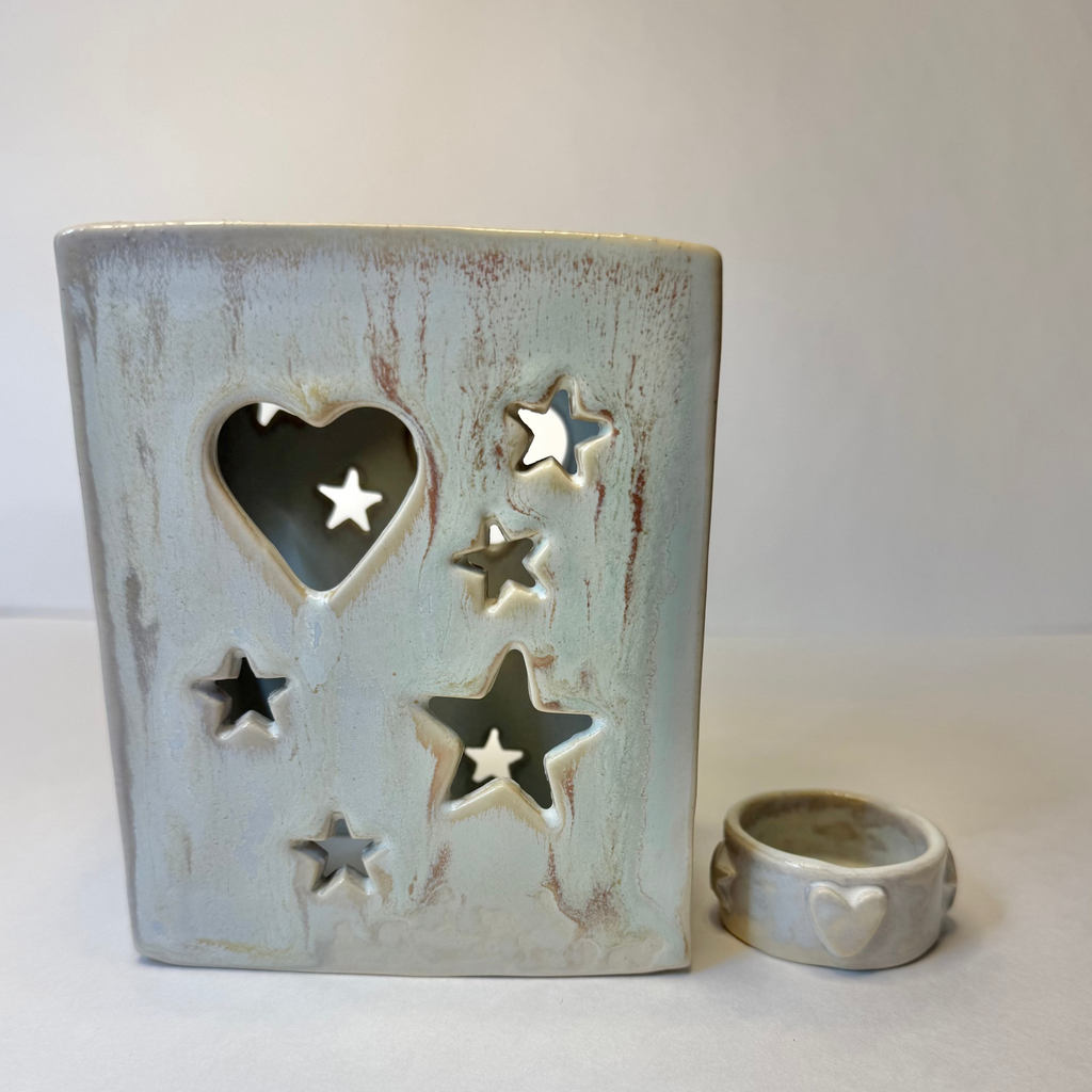 A ceramic heart-shaped candle holder with star cutouts, shown next to a matching small ring holder, both in a distressed light blue-gray glaze on a neutral background.