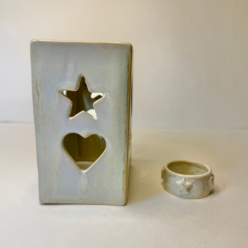 A rectangular ceramic candle holder with star and heart cutouts, shown next to a matching small ring holder, both in a light blue-gray glaze on a neutral beige background.
