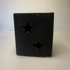 A square black decorative object with two star-shaped cutouts on the front, photographed against a plain light gray background.