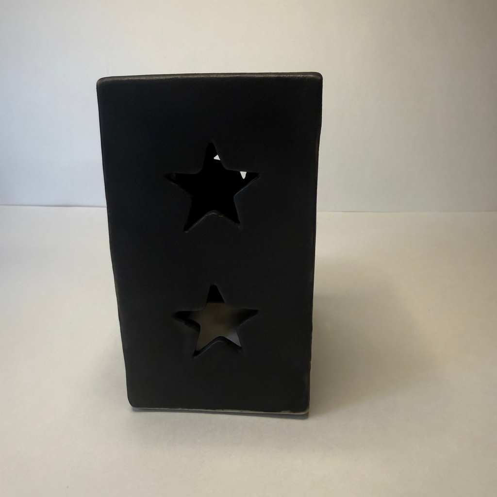 A black rectangular ceramic candle holder with two star-shaped cutouts, standing on a light gray surface against a neutral gray background.