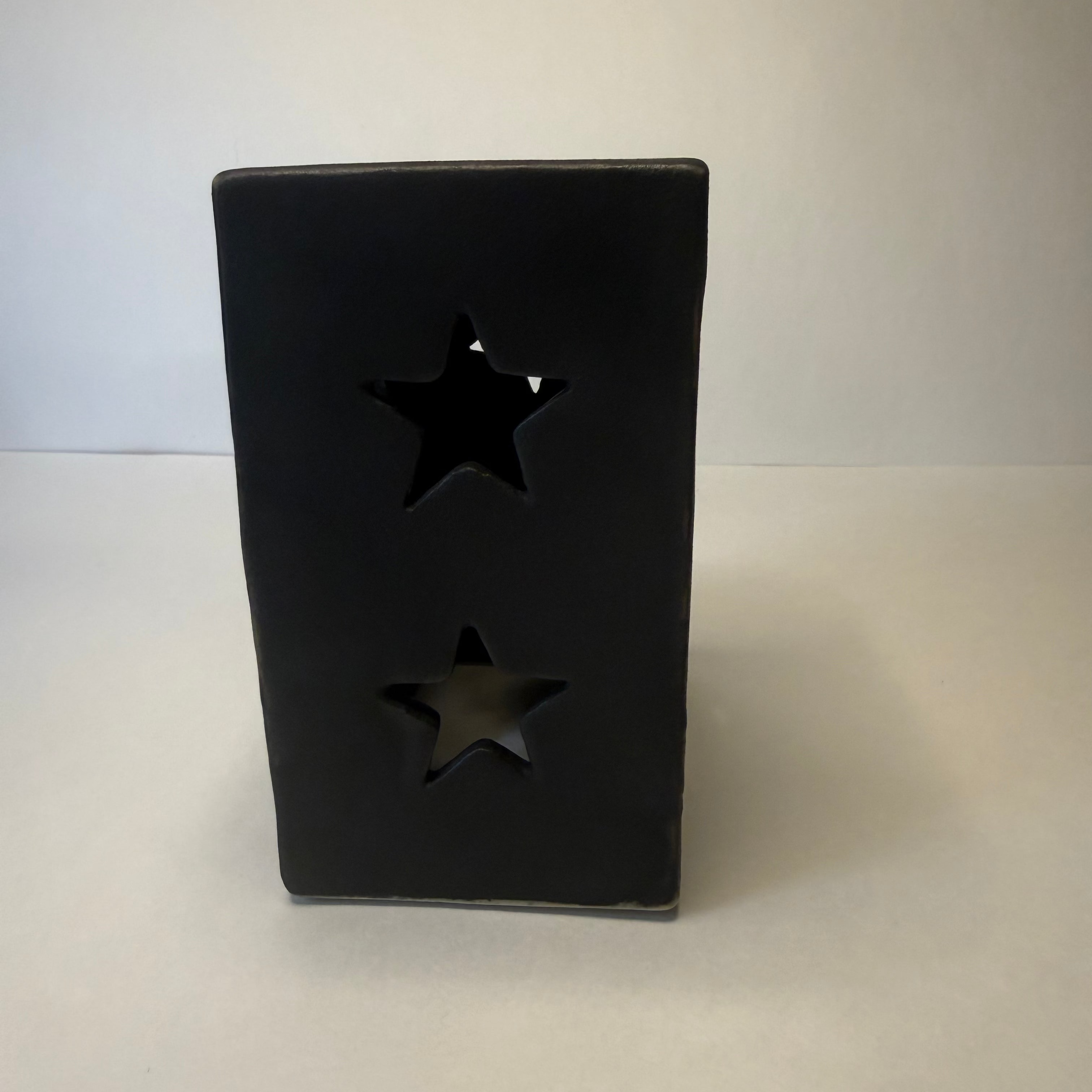 A black rectangular ceramic candle holder with two star-shaped cutouts, standing on a light gray surface against a neutral gray background.