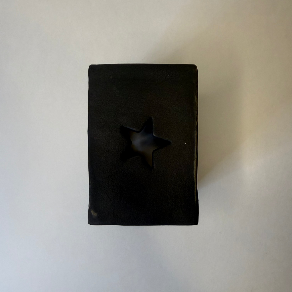 A matte black rectangular ceramic candle holder with a star-shaped cutout in the center, shown on a plain off-white background.