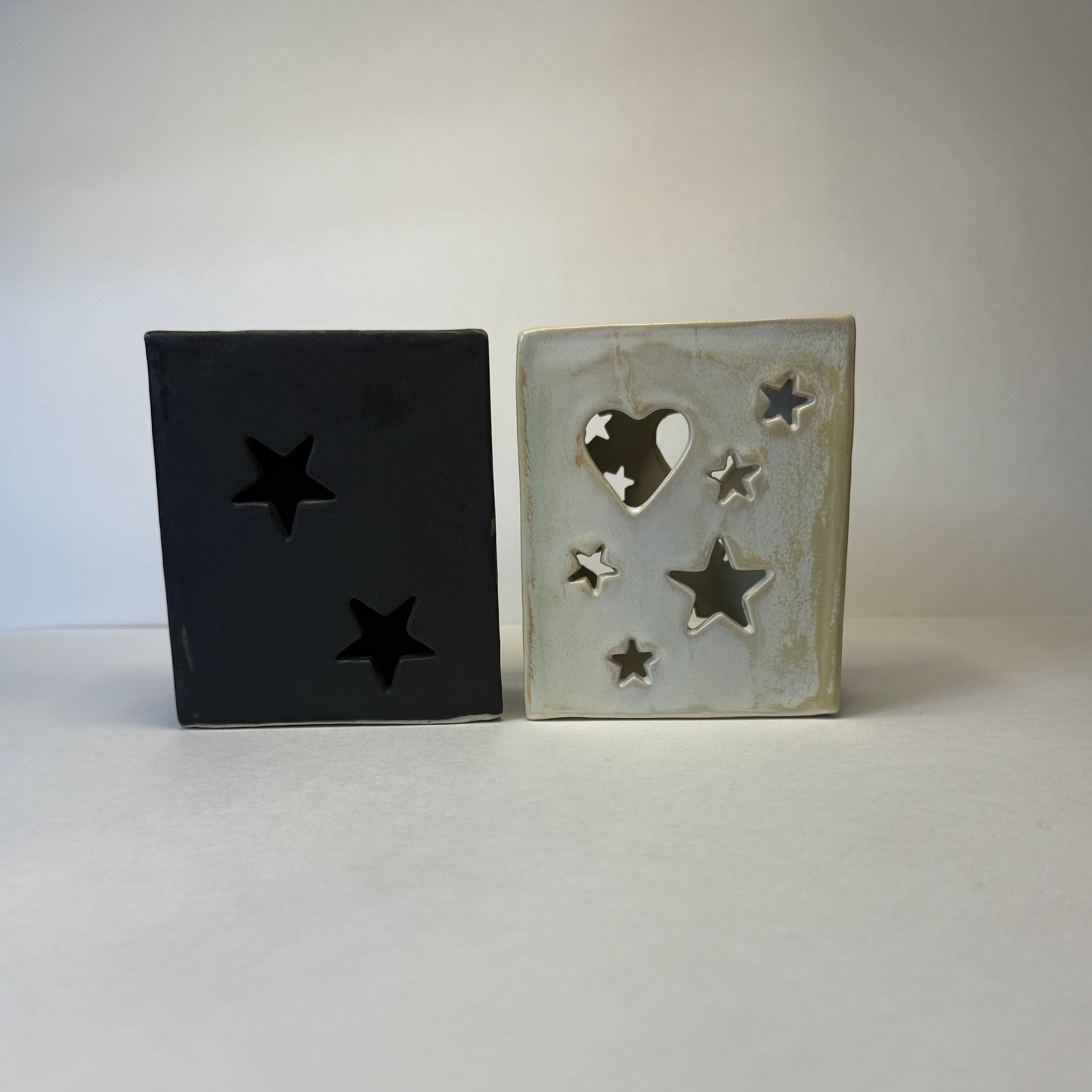 Two square ceramic decorative lanterns with star and heart cutouts, shown side by side on a white surface against a light gray background.