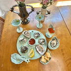 Celadon colored oyster platter with matching colored martini glasses and cups shaped like oysters. Two vases holding flowers and small oyster dishes holding crackers and ceramic spoons. 