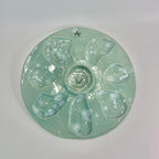 A round, glossy ceramic plate with oyster shape cut outs with a light mint green glaze and raised mini bowl for mignottes and sauces, photographed from above on a plain light background