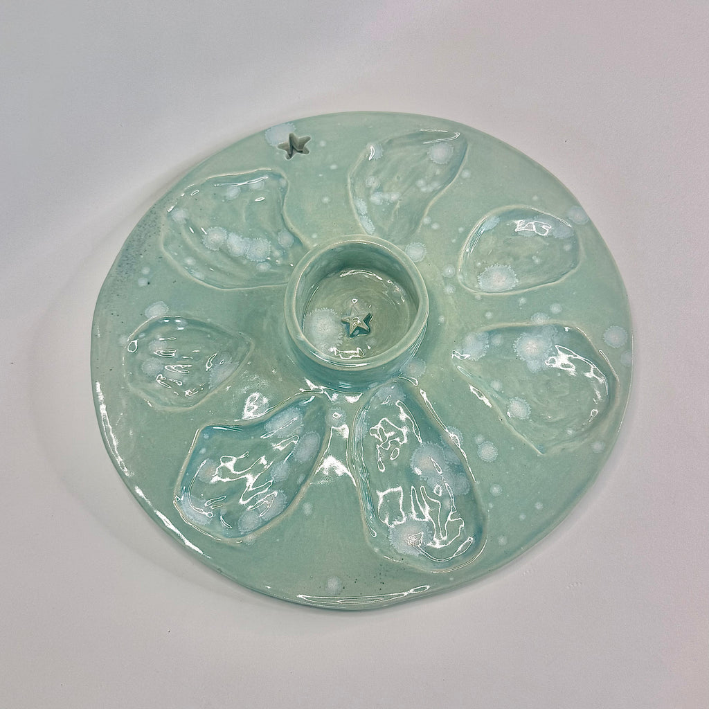 A round ceramic plate with a pale mint green glaze and five raised petal-like sections surrounding a central well, photographed on a plain light background.