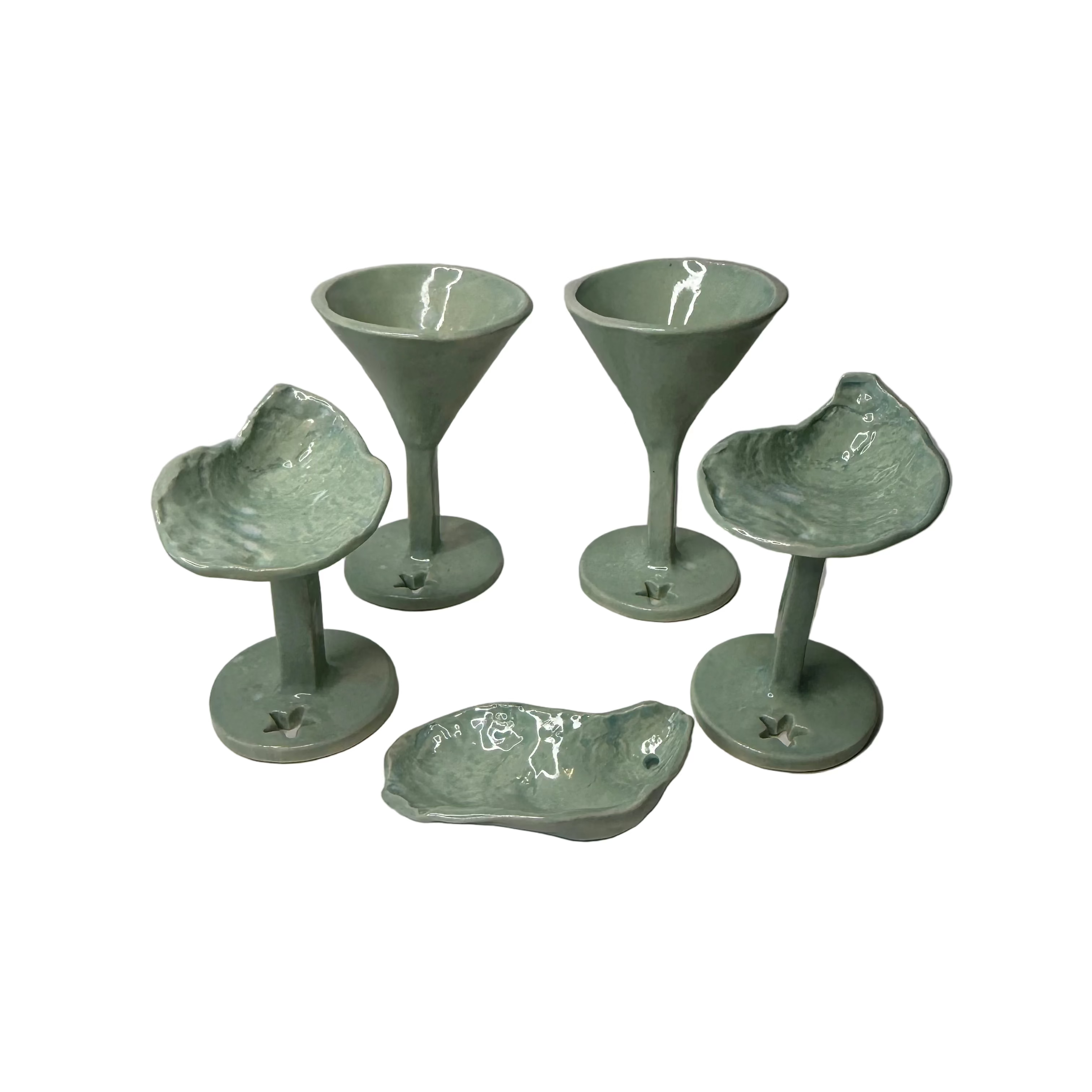 A set of five glossy pale green ceramic drinkware pieces on a plain white background, including two martini-style glasses, two stemmed goblets with sculpted textured oysters, and one small dish.